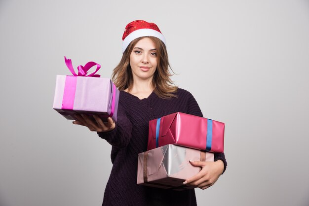 Presenta mujer joven con sombrero de Santa dando cajas de regalo.