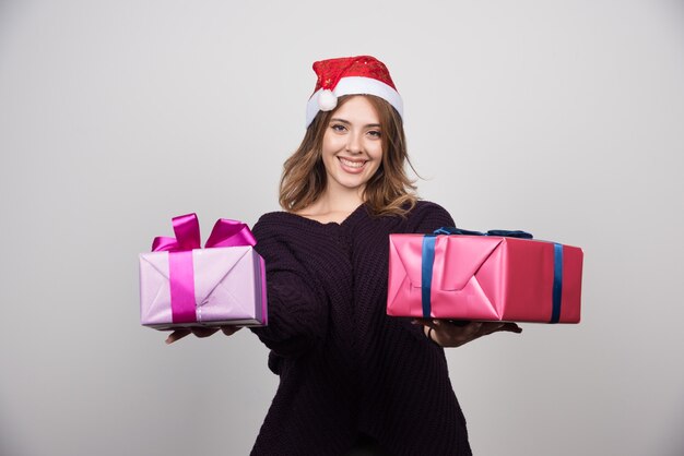 Presenta mujer joven con sombrero de Santa que ofrece cajas de regalo.