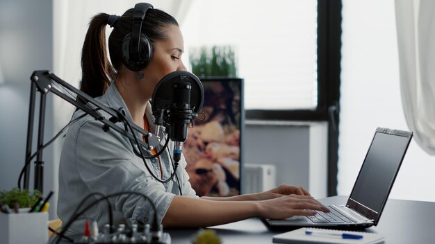 Presentador de podcast escribiendo en una laptop mientras habla con la audiencia. Creador de contenido creativo popular en Internet que chatea con el público en chat en vivo mientras habla con un micrófono moderno.