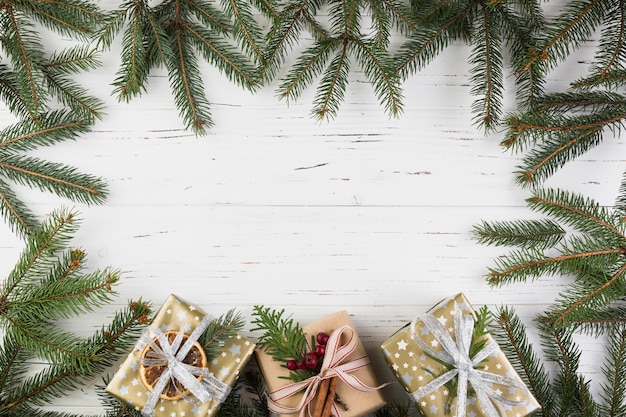 Presentar cajas en envoltura navideña cerca de ramas de abeto.