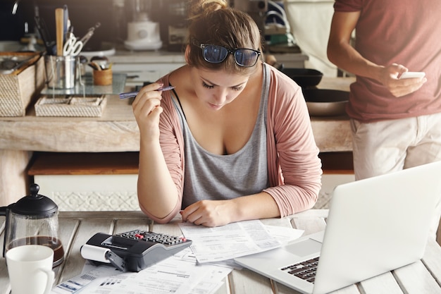 Foto gratuita presupuesto familiar y problemas económicos. mujer preocupada concentrada haciendo papeleo en casa, calculando gastos domésticos y pagando facturas de gas y electricidad, usando computadora portátil y calculadora