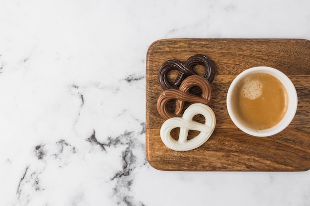 Pretzels de chocolate y taza de café en tajadera sobre fondo de mármol con textura