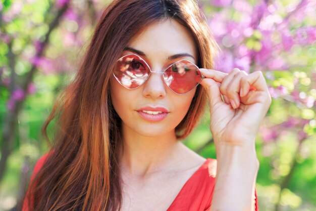 Primavera al aire libre cerca retrato de mujer morena disfrutando de flores en el soleado jardín floreciente.