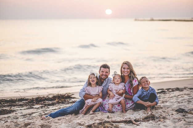 Primer disparo de una familia feliz sentada en la orilla del mar al atardecer - concepto de familia