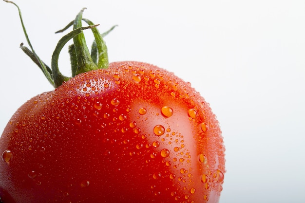 Primer disparo de un tomate fresco con gotas de agua aislado sobre un fondo blanco.