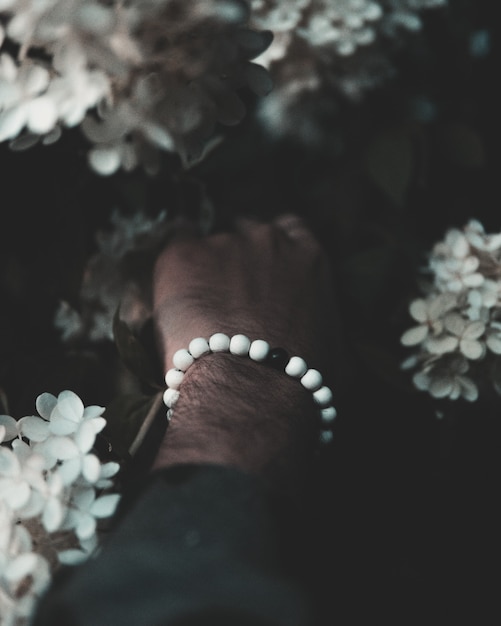 Primer disparo vertical de la mano de un hombre con cuentas blancas y negras tocando hermosas flores