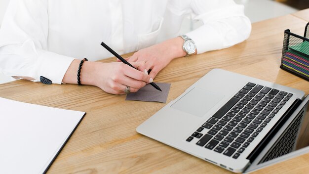 Primer de la escritura de la empresaria en nota adhesiva con la pluma sobre el escritorio de madera