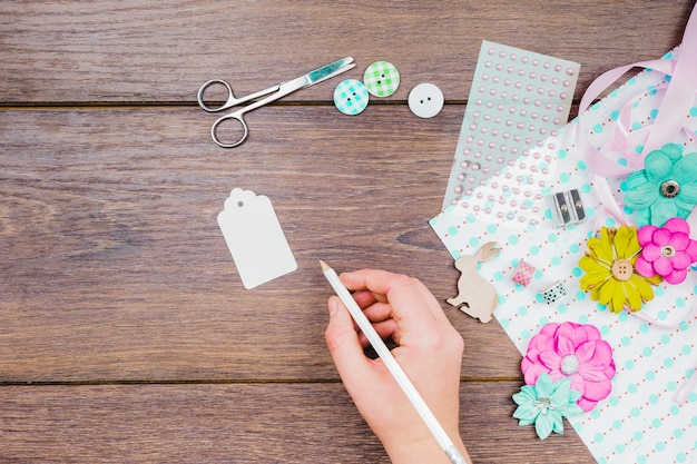 Foto gratuita primer de la escritura de la mujer en la etiqueta blanca con los botones; flores; tijera y artículos decorativos en mesa de madera.