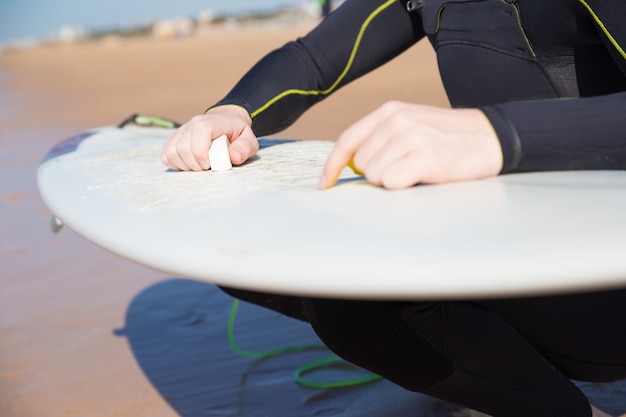 Foto gratuita primer del hombre joven que encera la tabla hawaiana en la playa soleada