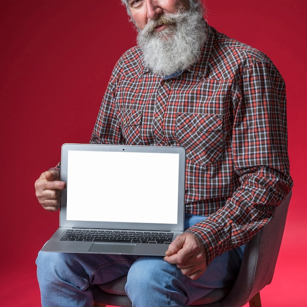 Primer del hombre mayor que muestra la tableta digital con la pantalla de visualización en blanco en blanco contra el contexto rojo