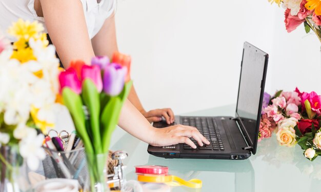 Primer de una mano femenina del florista que trabaja en la computadora portátil