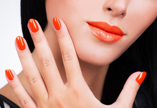 Primer mano femenina con hermosas uñas de color naranja en el rostro de la mujer