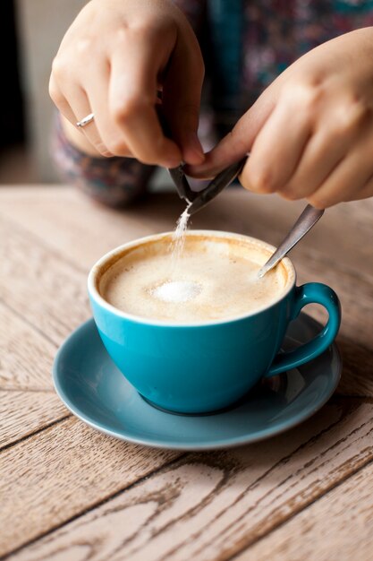 El primer de la mano femenina vierte el azúcar en el café sobre superficie de madera