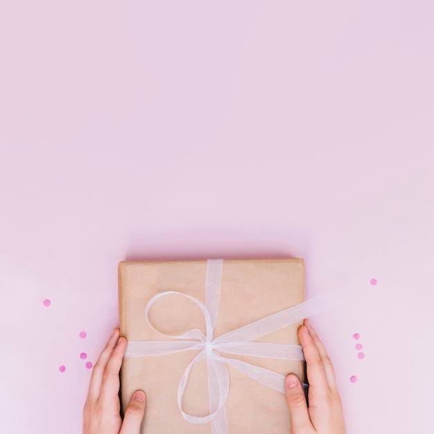 El primer de la mano que lleva a cabo cumpleaños envolvió la caja de regalo con la cinta blanca en fondo rosado