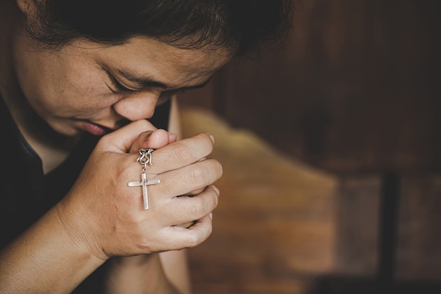 El primer de las manos mayores cristianas de la mujer que sostienen la cruz crucificada mientras que ruega a dios.