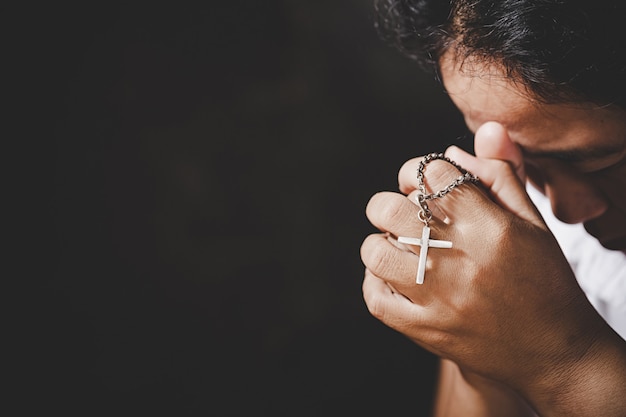 El primer de las manos mayores cristianas de la mujer que sostienen la cruz crucificada mientras que ruega a dios.