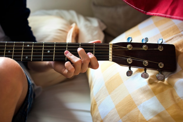 Primer del muchacho caucásico joven que toca la guitarra en cama