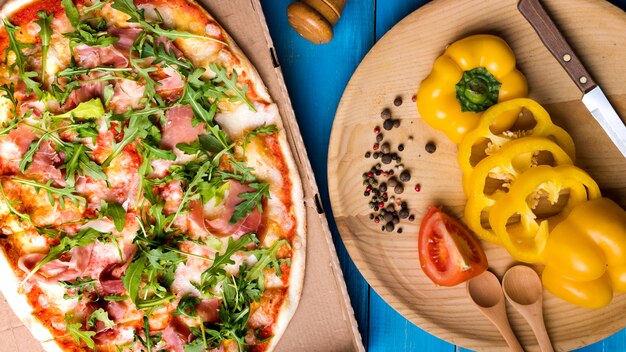 El primer de la pizza con tocino y arugula se va cerca de la pimienta cortada; tomate; ajo y especias sobre mesa