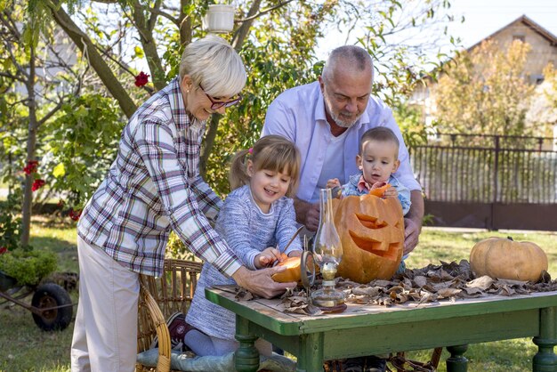Primer plano de abuelos ayudando a los niños a tallar una calabaza para Halloween