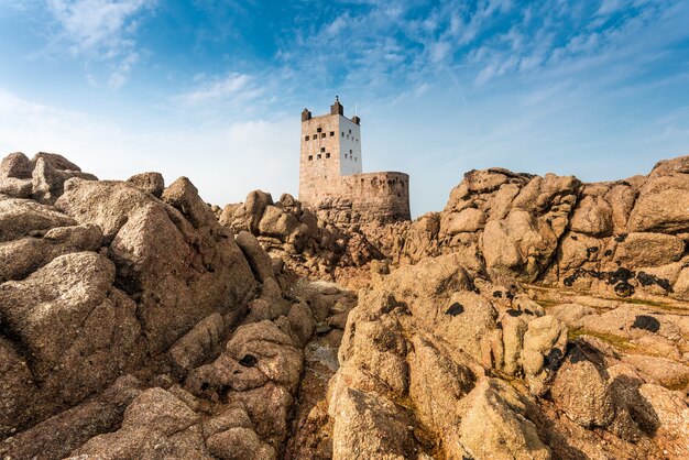 Primer plano de acantilados y rocas con una fortaleza en el fondo bajo un cielo azul