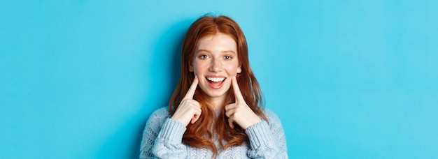 Foto gratuita primer plano de una adolescente alegre con pelo rojo y pecas metiendo las mejillas mostrando hoyuelos y sonriendo