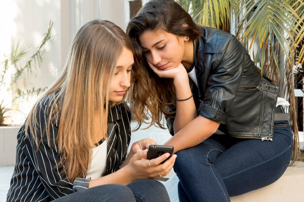 Primer plano de una adolescente bonita que muestra el teléfono celular a su amiga