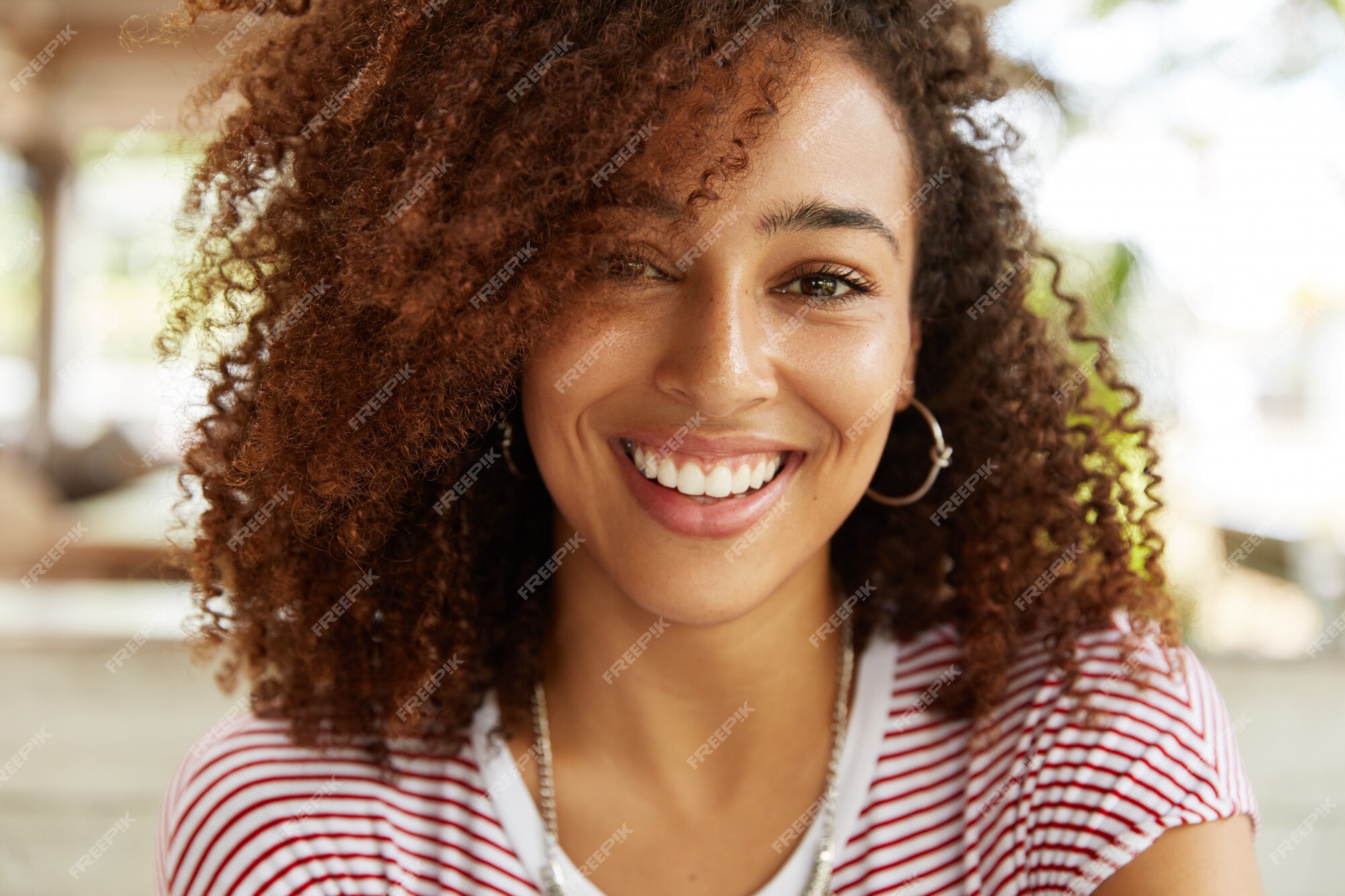 Primer plano de una adorable mujer afroamericana tiene una amplia sonrisa,  viste una camiseta a rayas, está de buen humor, descansa en la cafetería  con los mejores amigos. sonriente mujer joven de