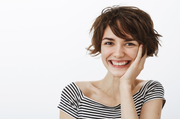 Primer plano de una adorable mujer morena riendo y ruborizándose de cumplido, sonriendo tontamente