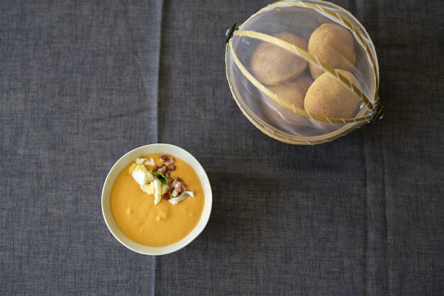 Primer plano aéreo de una salsa de sopa de naranja en un recipiente blanco con pan sobre un mantel negro