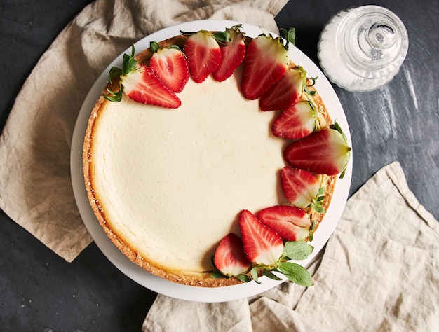 Primer plano aéreo de una tarta de queso con fresas en una placa blanca.
