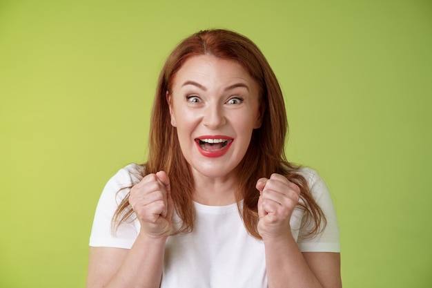 Primer plano afortunado entusiasta linda pelirroja alegre mujer de mediana edad puños de bomba vigoroso entusiasmo celebratorio sonriendo ampliamente ganando celebrando triunfante éxito buenas noticias