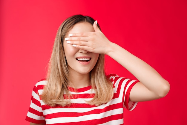 Primer plano afortunado linda mujer rubia asiática sonriendo ampliamente contar diez prometer no asomarse cubrir los ojos con la palma de la mano ...