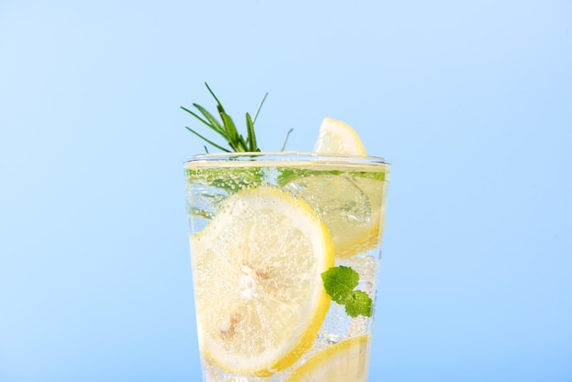 primer plano de agua de limón fresca en vaso con rebanadas de limón frutas aisladas en fondo azul