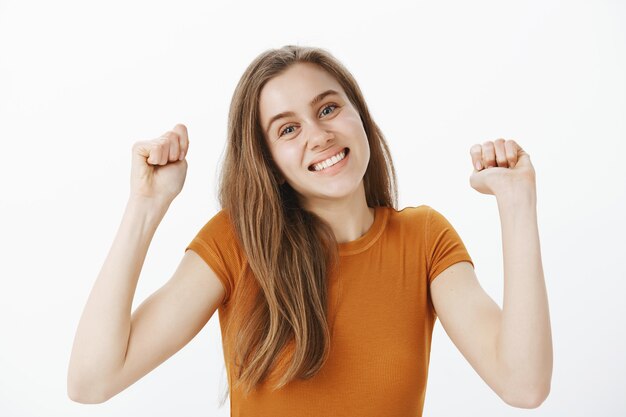 Primer plano de alegre linda joven regocijándose, levantando las manos en gesto de hurra, bomba de puño y sonriendo, triunfando sobre la victoria