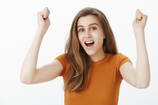 Primer plano de alegre linda joven regocijándose, levantando las manos en gesto de hurra, bomba de puño y sonriendo, triunfando sobre la victoria