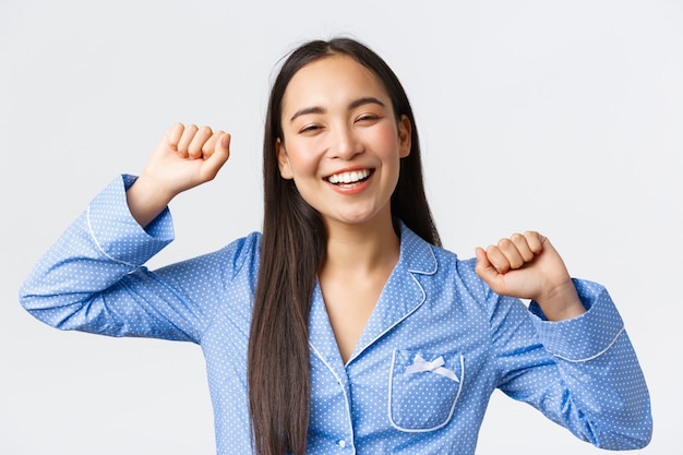 Primer plano de una alegre niña asiática sonriente despertando optimista y estirándose con cara feliz, tuvo un gran sueño nocturno, sintiéndose lleno de energía a partir de la mañana con una sonrisa, fondo blanco