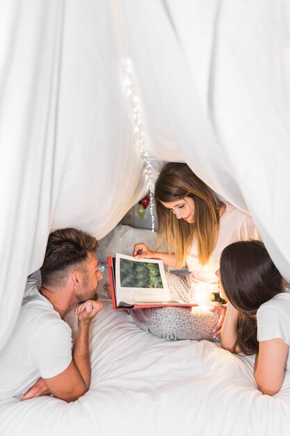 Primer plano de amigos leyendo el libro sentado en la cama bajo la cortina