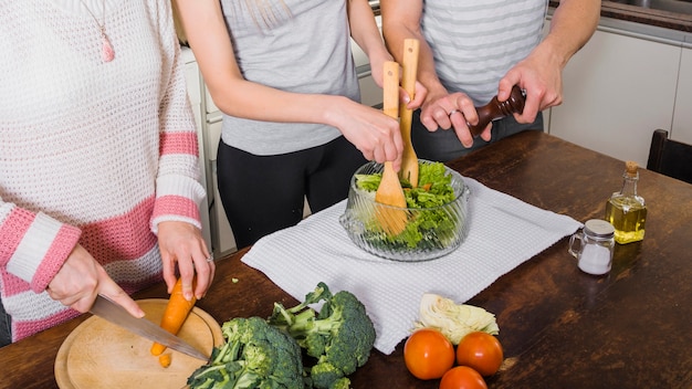 Primer plano de amigos preparando ensalada de verduras frescas en la mesa de madera