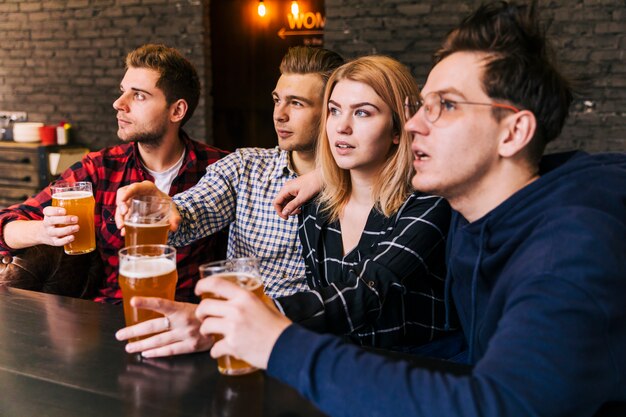 Primer plano de amigos sosteniendo los vasos de cerveza mirando a otro lado