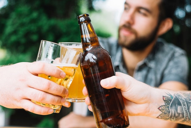 Primer plano de amigos varones que anima con bebidas alcohólicas al aire libre