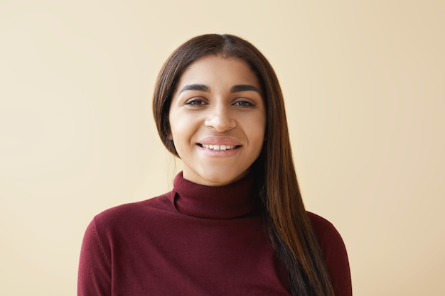 Primer plano de amistoso aspecto elegante joven mujer afroamericana con cabello lacio recto oscuro con mirada feliz y alegre posando