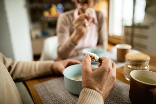 El primer plano de un anciano comiendo galletas mientras desayuna con su esposa en casa