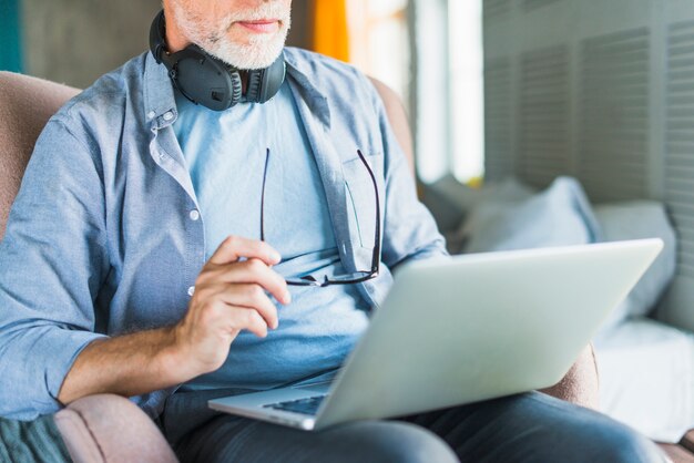 Primer plano, de, anciano, hombre, tenencia, gafas, usar la computadora portátil