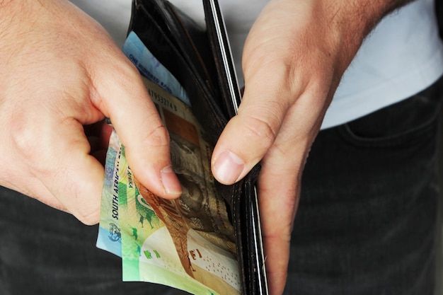 Primer plano de ángulo alto de una persona poniendo algo de dinero en efectivo en una billetera de cuero