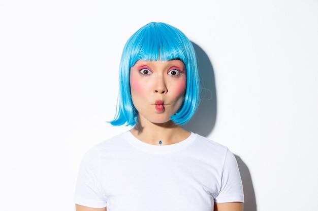 Foto gratuita primer plano de animadora asiática divertida y tonta celebrando halloween, con peluca azul, mostrando muecas.