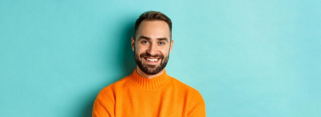 Primer plano de un apuesto hombre caucásico sonriendo a la cámara mirando confiado usando suplente de suéter naranja