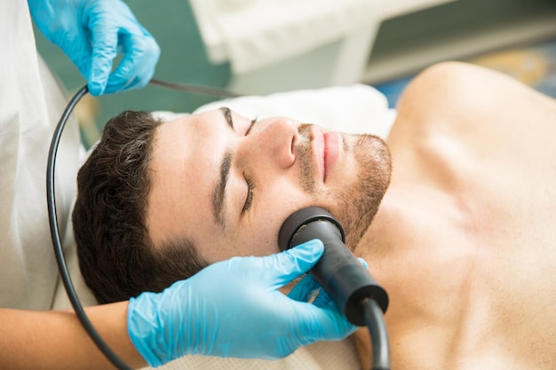 El primer plano de un apuesto joven que recibe terapia de rejuvenecimiento facial en un spa de salud