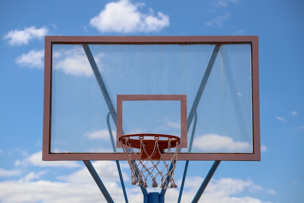 Primer plano de un aro de baloncesto en un campo bajo la luz del sol y un cielo azul