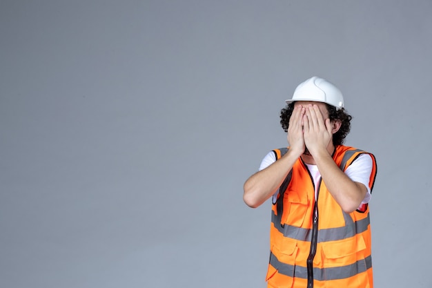 Foto gratuita primer plano del arquitecto masculino en chaleco de advertencia con casco de seguridad y cerrando su rostro sobre la pared gris de la ola