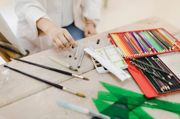 Primer plano de artista femenina con lápices de colores negros en la mesa de madera